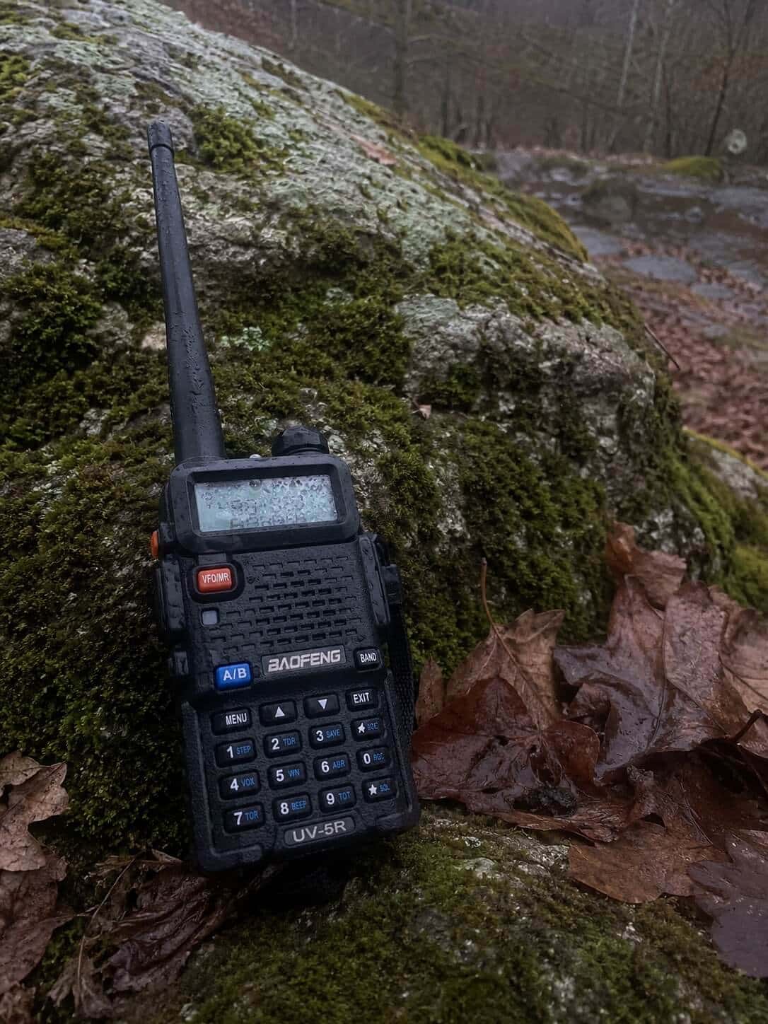 Wet Baofeng UV-5R resting on moss-covered rock with autumn leaves